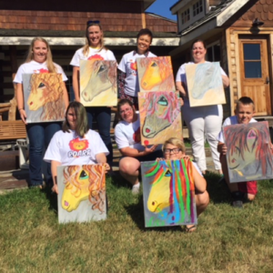 A group of people holding up paintings in front of a house.